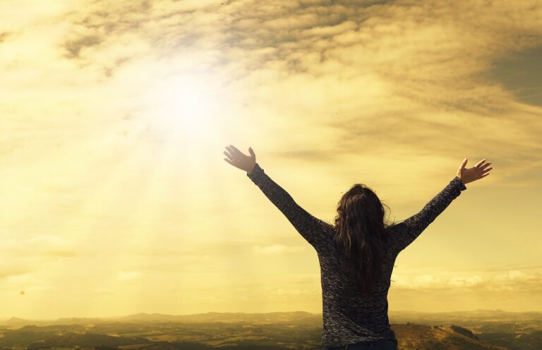 Mujer disfrutando del sol y del aire fresco en un campo con los brazos extendidos hacia el cielo.